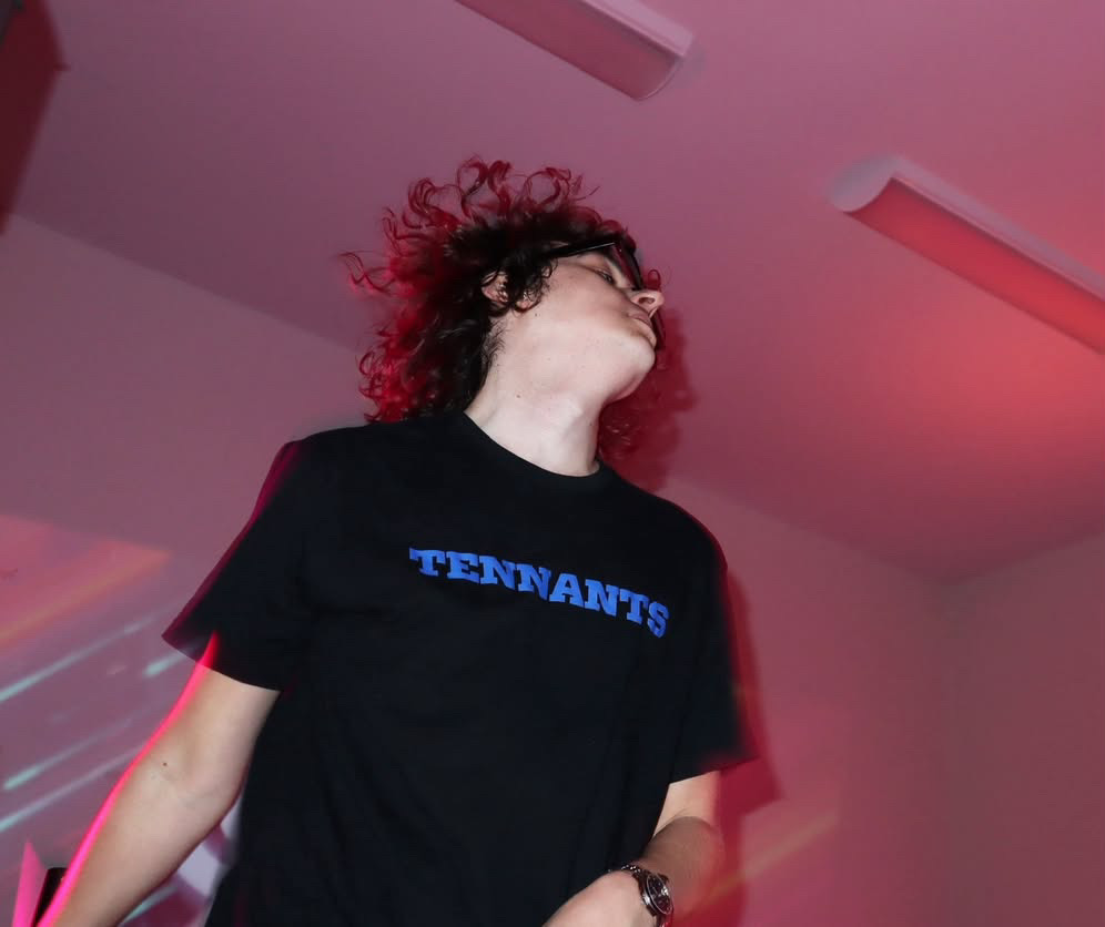 Tennants onstage under red lighting wearing a Tennants shirt